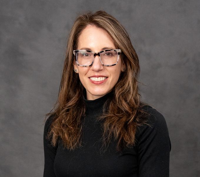 A woman with long dark hair and glasses in a black turtleneck.