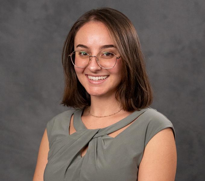 A woman with short dark hair and glasses in a grey top.