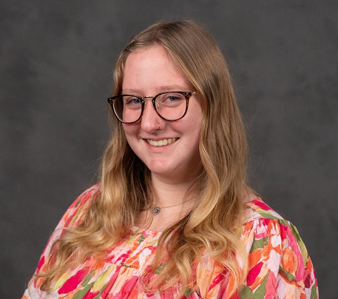 Photo of a woman with long blonde hair and glasses smiling in a pink floral top.