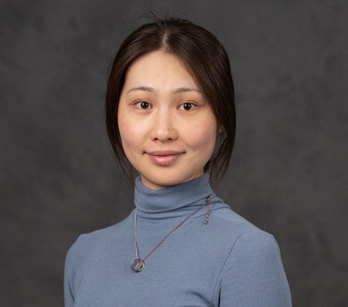 A woman with dark hair tied back in a blue turtle neck.