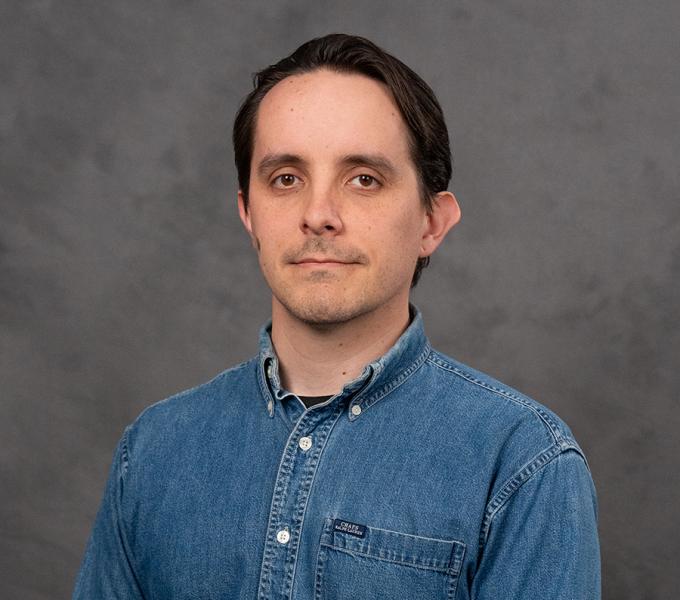 A man with short dark hair in a denim button down shirt.