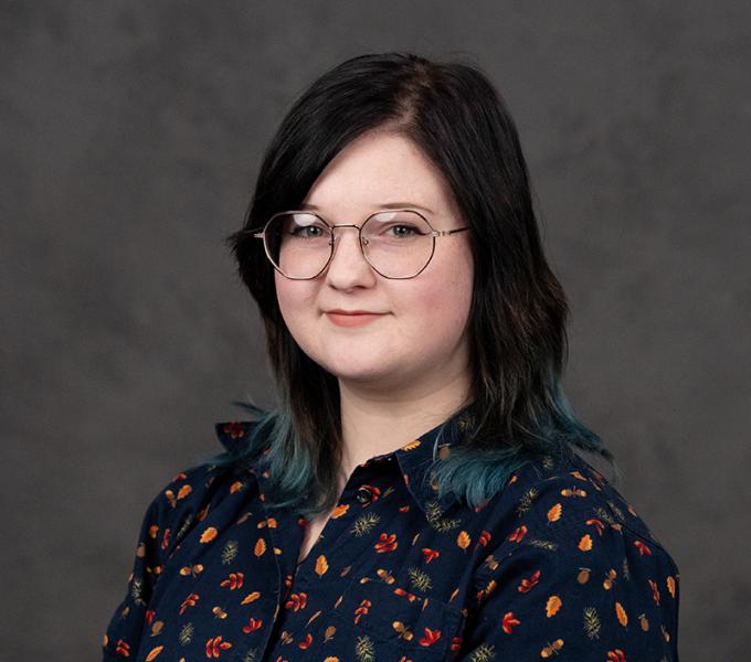 Photo of a woman with short dark hair and glasses smiling in a black floral top.