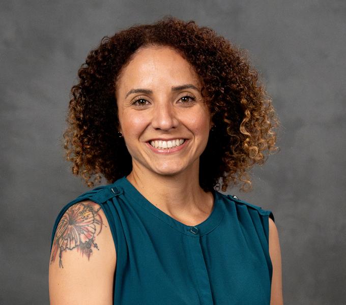 Photo of a woman with short curly hair in a dark green sleeveless blouse.