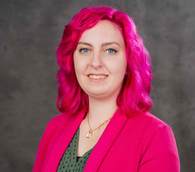 Headshot of a woman with hot pink hair, wearing a matching blazer.