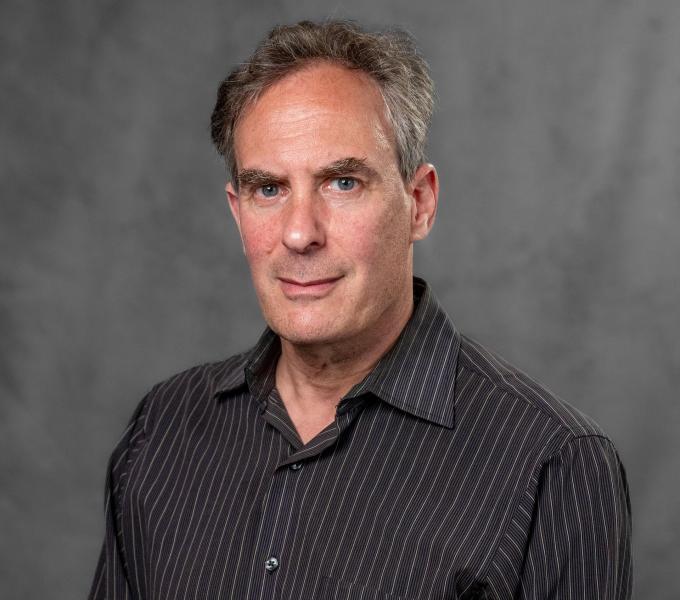 Headshot of a man with gray hair in a pinstriped charcoal button down shirt.