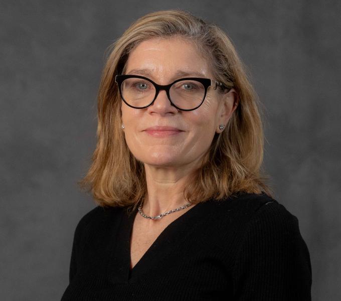 Headshot of a woman with shoulder-length blonde hair in a black v-neck blouse and matching black cat-eye glasses.