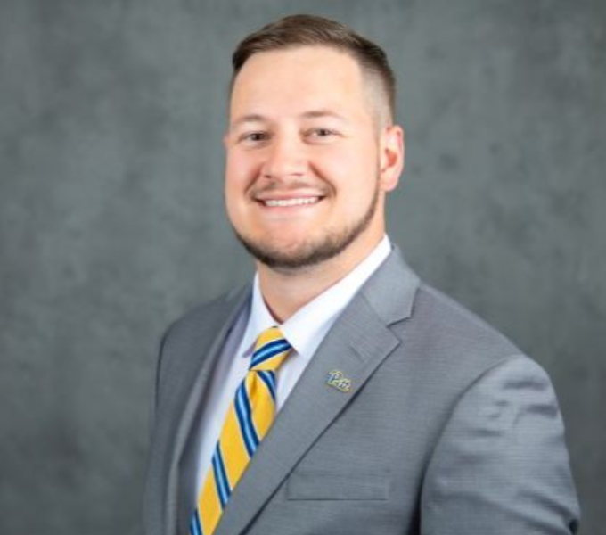 Headshot of smiling man in a gray blazer and yellow and blue striped tie.