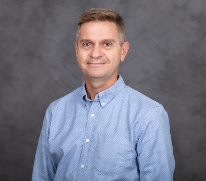 Headshot of a man in a light blue button down shirt.