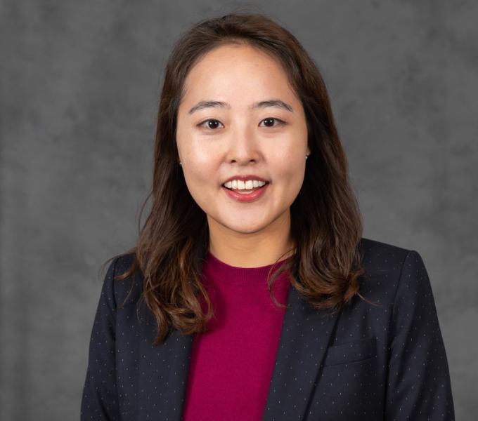 Headshot of a smiling woman in a merlot red shirt and black dotted blazer.