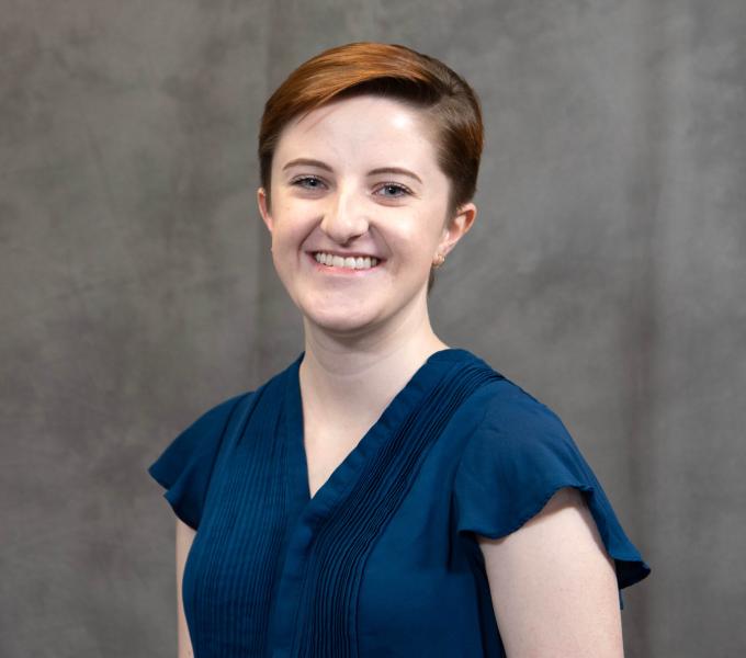 Headshot of a smiling woman with short shorn strawberry blonde hair in a dark blue shirt.