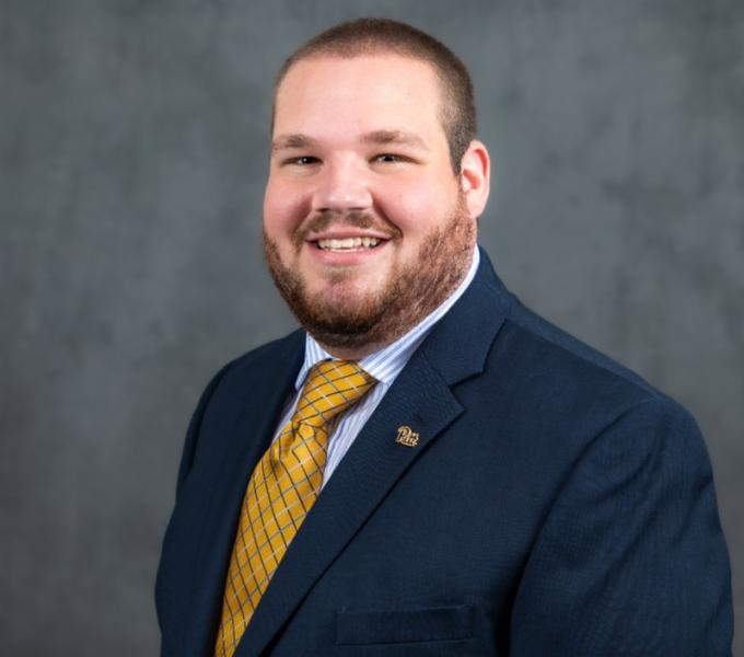 Headshot of smiling man in a navy blazer and gold-colored tie.