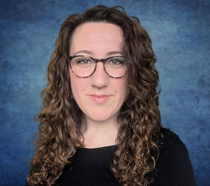 A photo of a woman with long curly hair and glasses smiling in a black top.