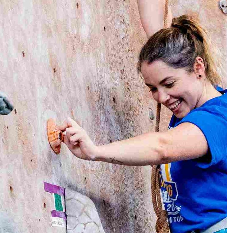 A young woman climbs up a stone interior climbing wall.